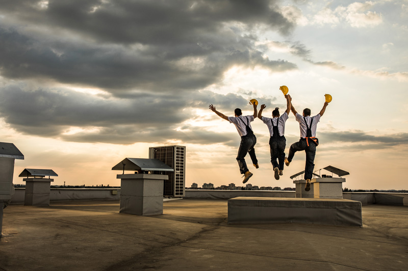 Drei Handwerker auf einem Dach springen vor Freude in die Luft